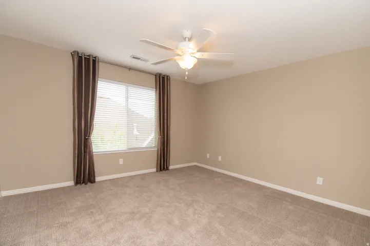 Spacious room featuring neutral wall paint, light-toned carpeting, a window with horizontal blinds, and a ceiling fan with integrated lighting