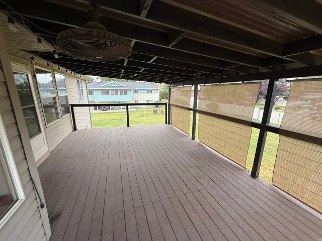Spacious covered deck featuring composite decking, black metal railings, and natural fiber shades