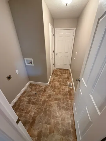 Functional laundry area featuring a sloped ceiling, brown-toned rectangular tile flooring, and light neutral wall paint