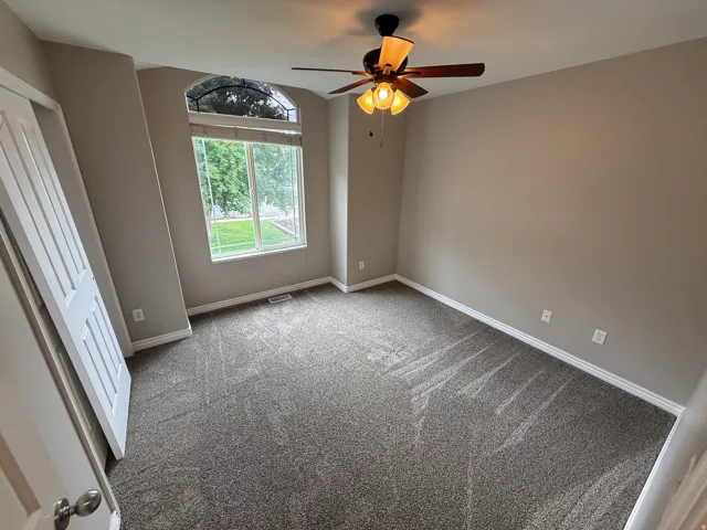 Carpeted room featuring a large arched window, ceiling fan with integrated lighting, white baseboards, and a paneled door