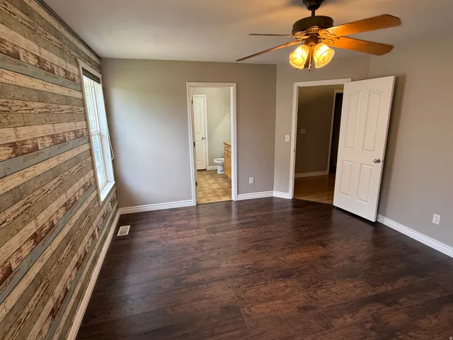 Room featuring wood-finish flooring, a decorative accent wall, and a ceiling fan with integrated lighting