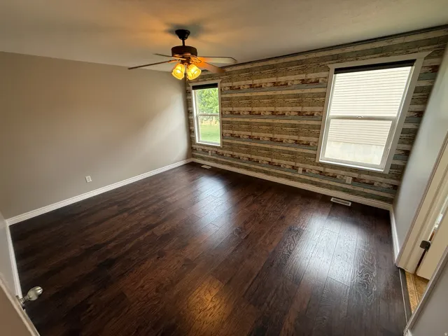 Spacious room featuring dark wood-finish flooring, a decorative accent wall with horizontal paneling, and a ceiling fan with integrated lighting