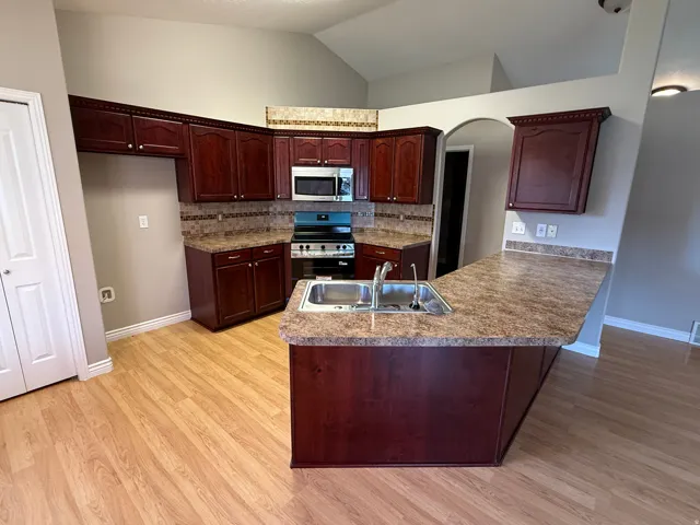 Kitchen featuring wood-finish flooring, dark wood cabinetry, a stainless steel double basin sink, and an integrated stainless steel microwave