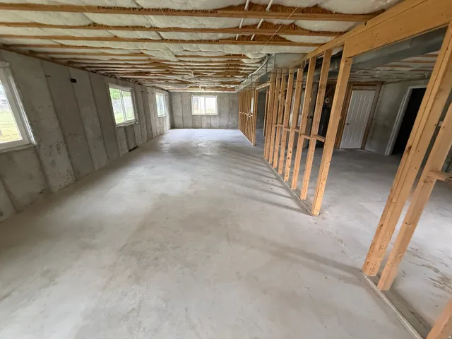 Unfinished basement featuring extensive concrete flooring, perimeter windows, exposed ceiling joists with insulation, and rough-in framing for future development