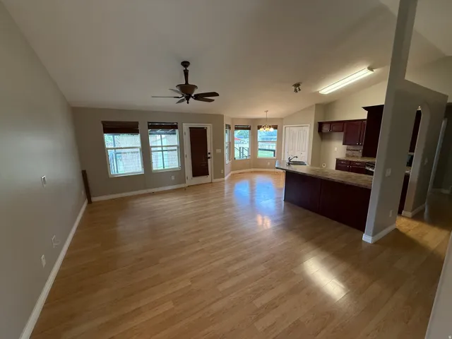 Open-concept living area featuring wood-finish flooring, a ceiling fan, and multiple windows with blinds