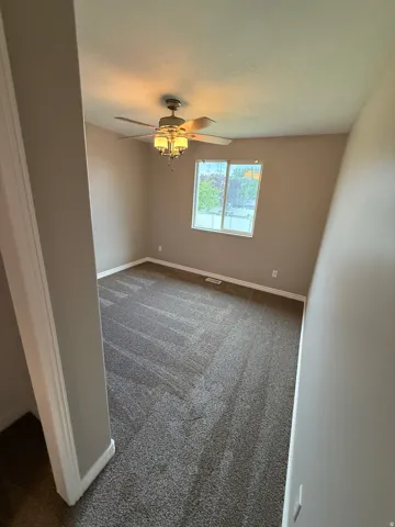 Carpeted room featuring a ceiling fan with integrated lighting, a double-hung window, and neutral wall paint