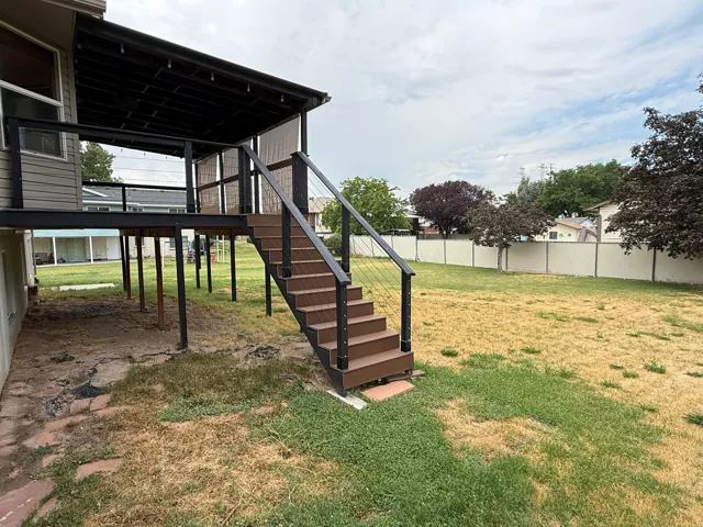 Expansive backyard with a covered elevated deck featuring a cable railing system and stair access