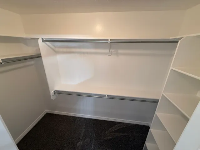 Walk-in closet featuring built-in shelving, dual hanging rods, and dark carpet flooring
