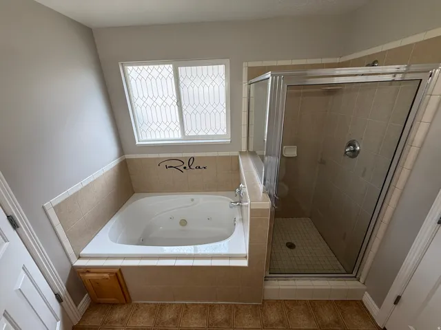 Soaking tub with tiled surround, a glass-enclosed shower, and a decorative privacy window