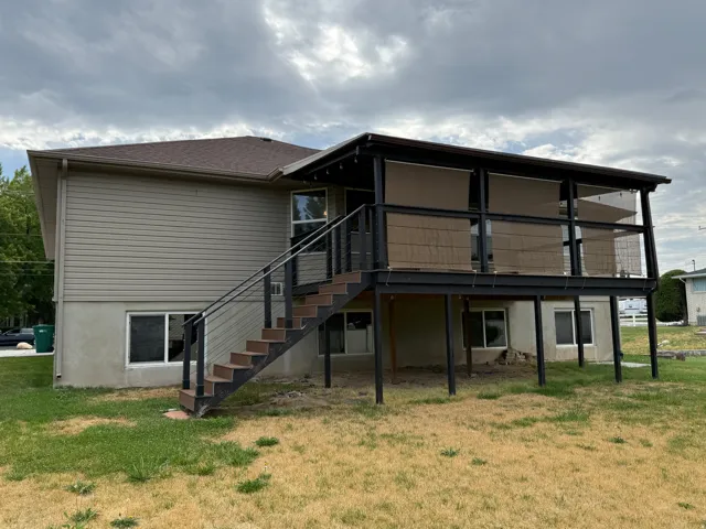 Rear exterior featuring a covered deck with retractable screens, a dark-toned staircase with metal railings, and a lower-level concrete foundation