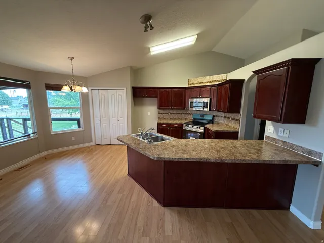 Open-concept kitchen and dining area featuring wood-finish flooring, vaulted ceilings, and extensive wood cabinetry