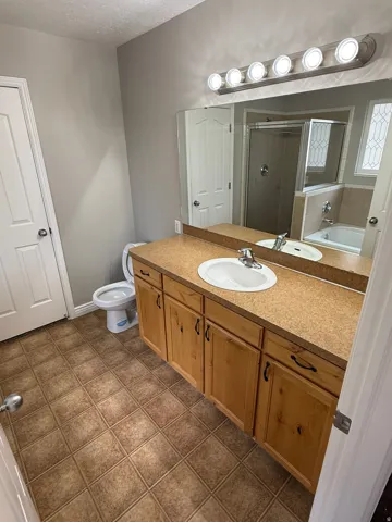 Bathroom featuring a double vanity with light wood cabinetry and a speckled countertop