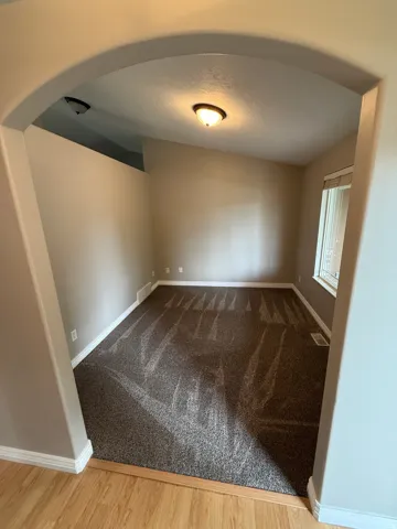 Arched entryway leading to a room with patterned carpeting, neutral wall tones, and a single window with vertical blinds