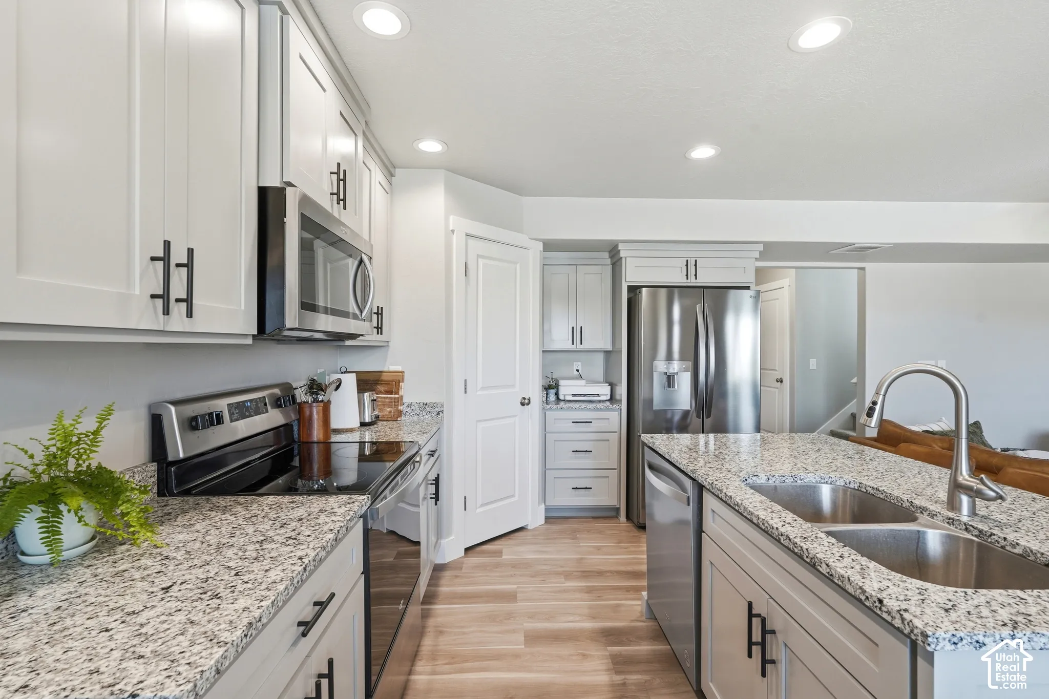 Modern kitchen featuring light cabinetry with dark hardware, speckled countertops, stainless steel appliances, and wood-finish flooring