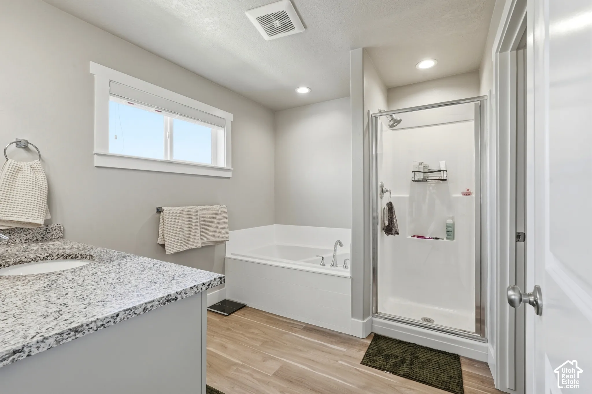 Primary Bathroom featuring a built-in soaking tub, glass-enclosed shower, single vanity with a granite-style countertop, and wood-finish flooring