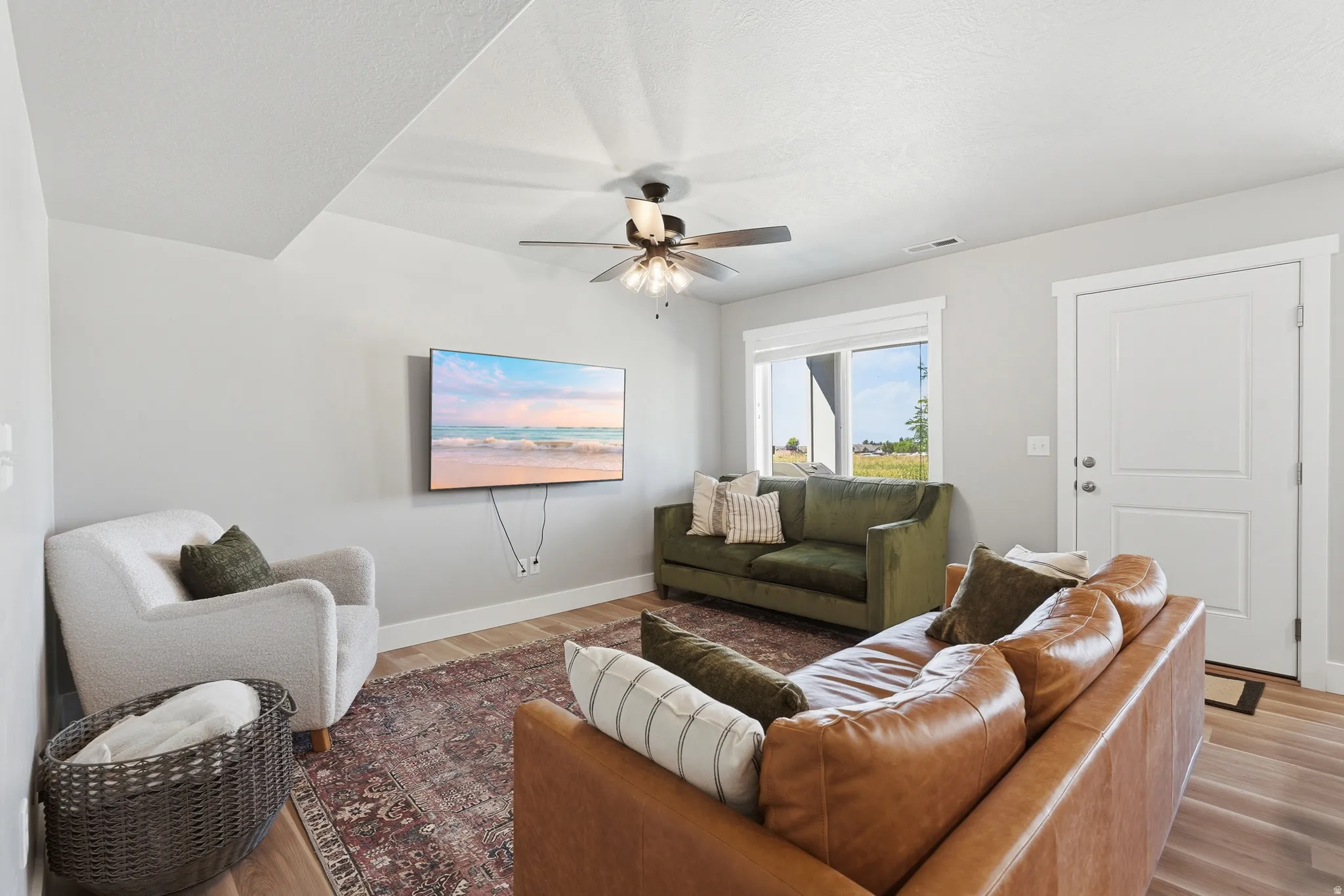 Open-concept living space with light gray walls, wood-finish flooring, and a ceiling fan