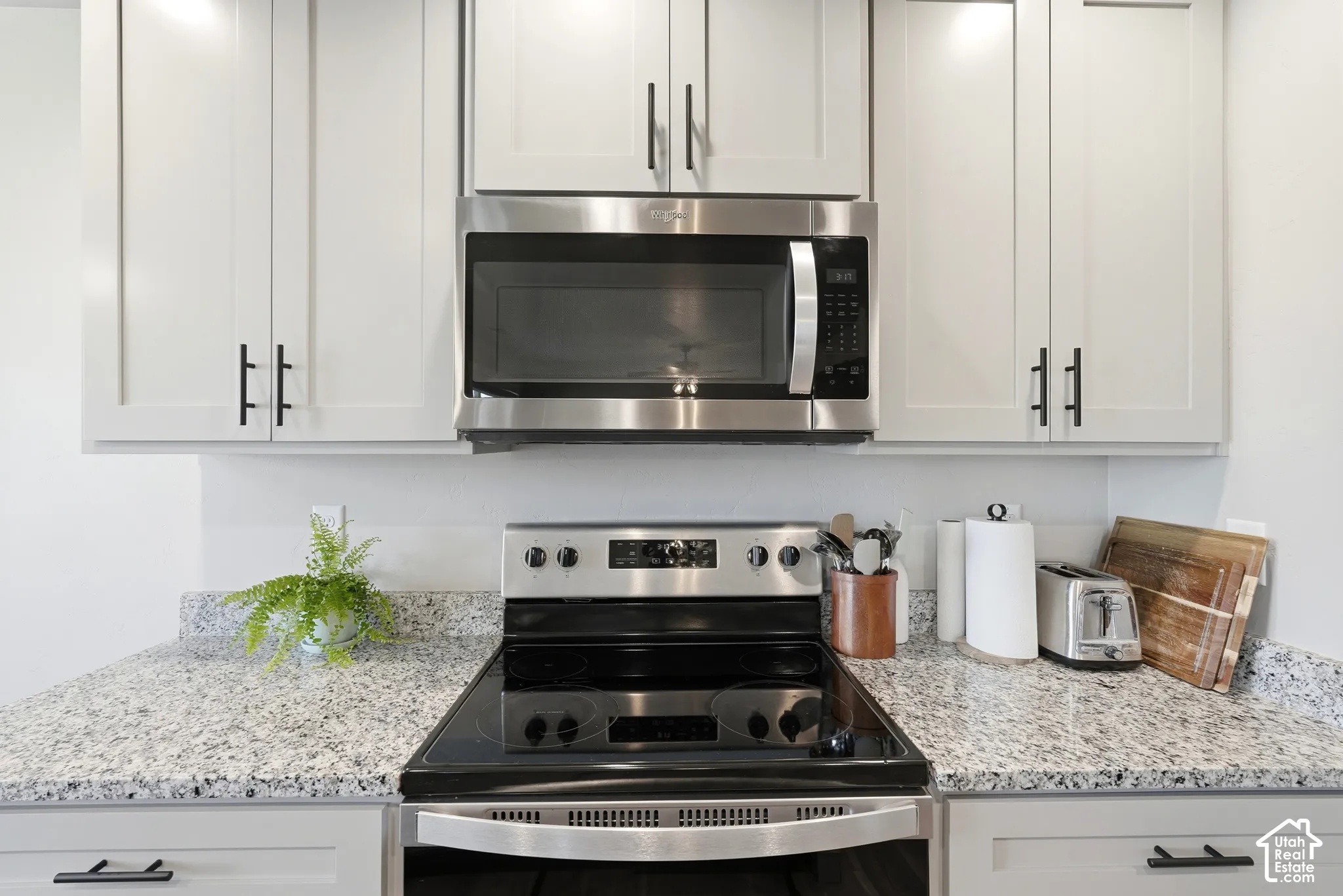 Kitchen featuring light gray cabinetry, stainless steel appliances, speckled stone countertops, and black hardware