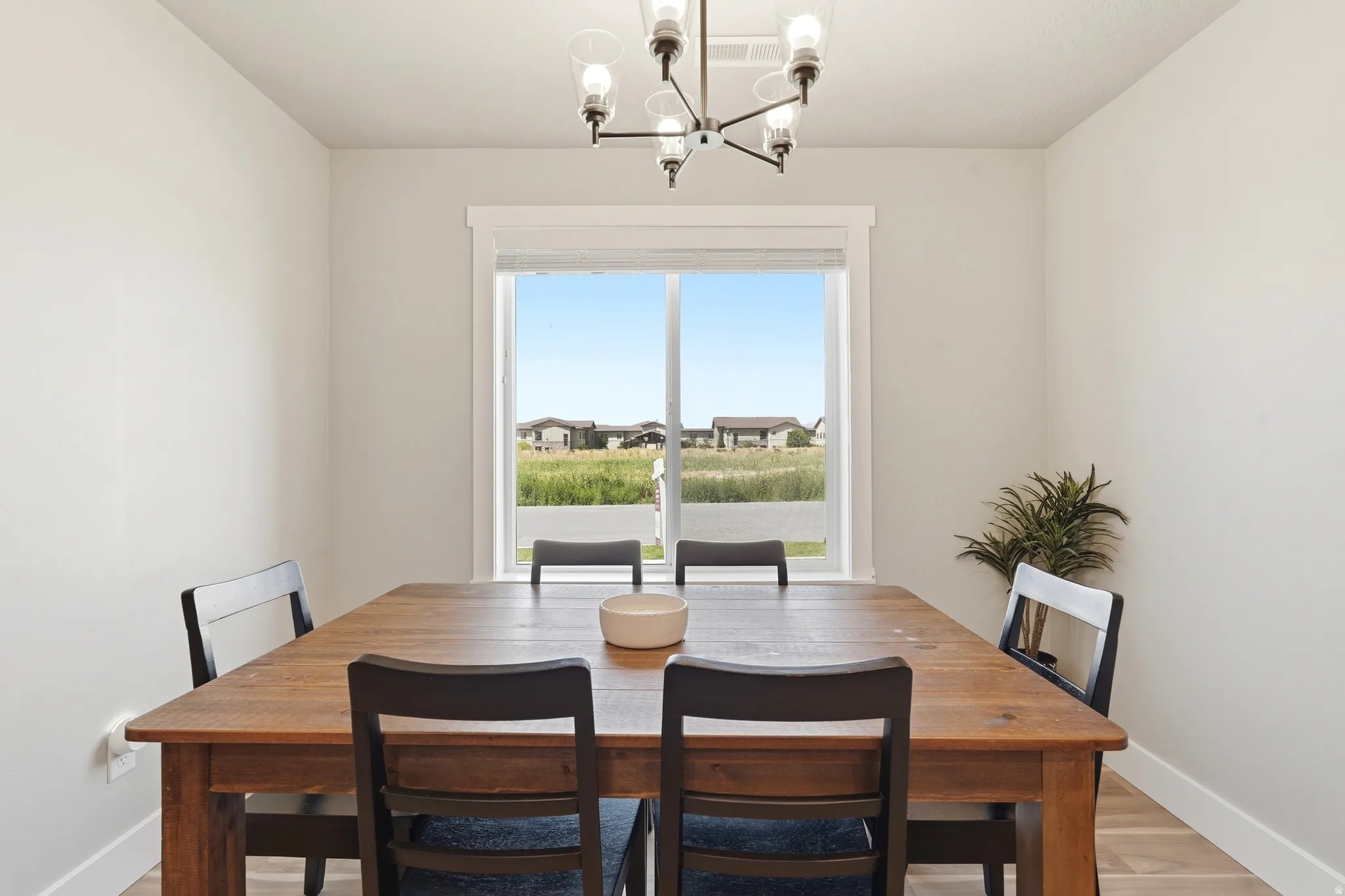Dining area featuring a modern chandelier with clear glass shades, a large window with white trim, light-toned walls, and wood-finish flooring