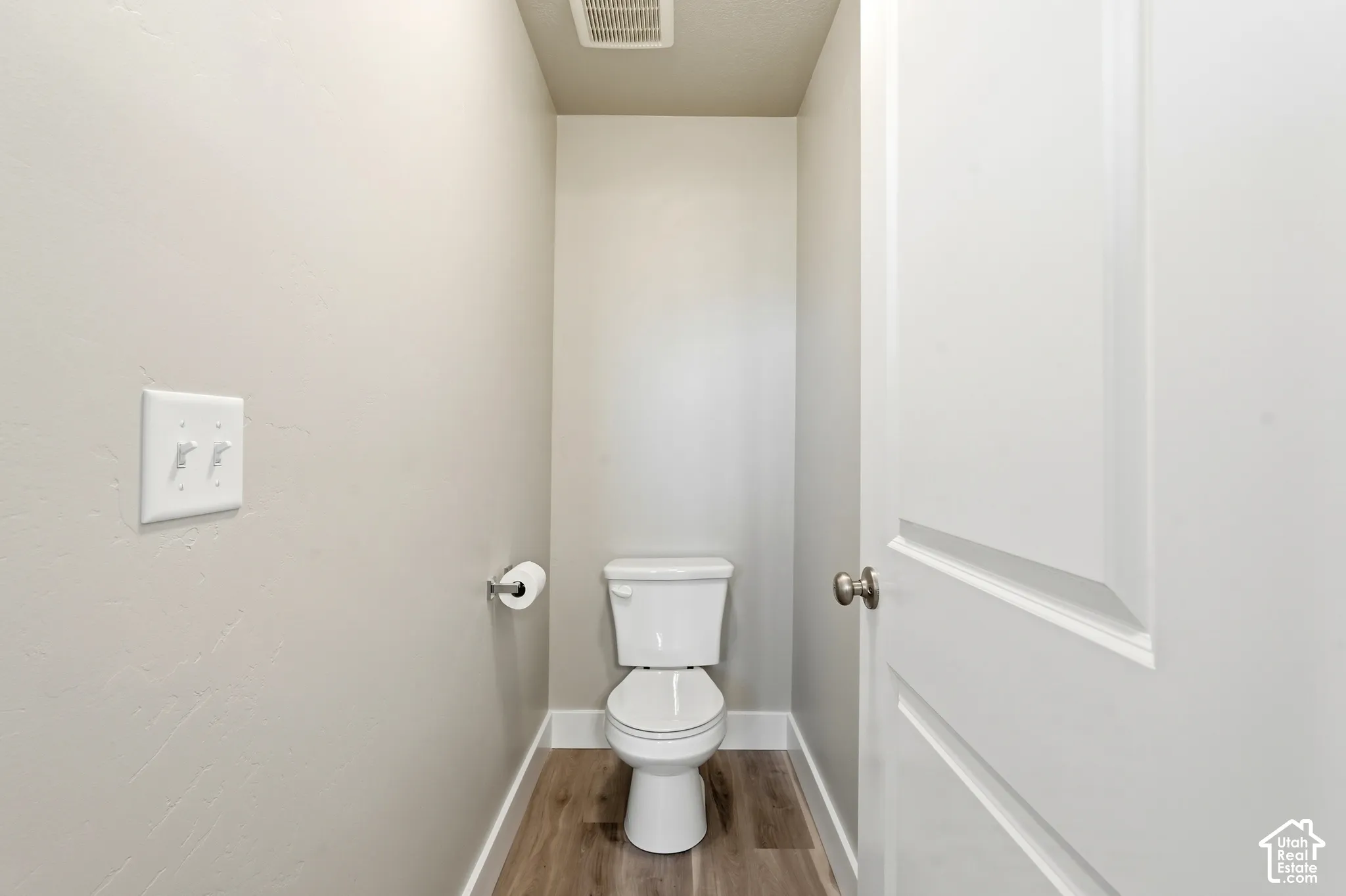 Primary toilet room featuring neutral wall tones, white trim, wood-finish flooring, and a panel-style door
