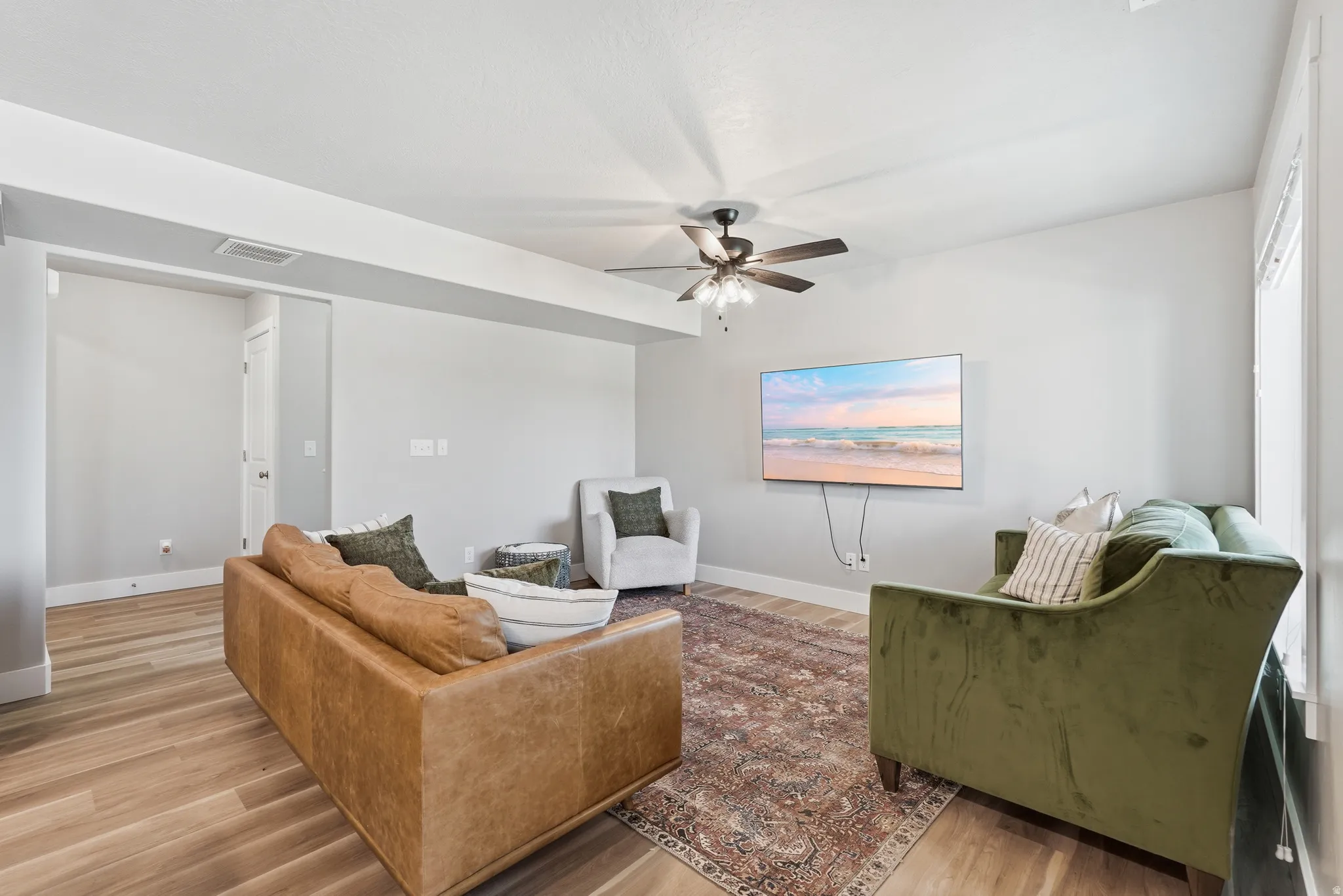 Spacious living area featuring wood-finish flooring, a ceiling fan, light gray walls, white trim, and an open entryway