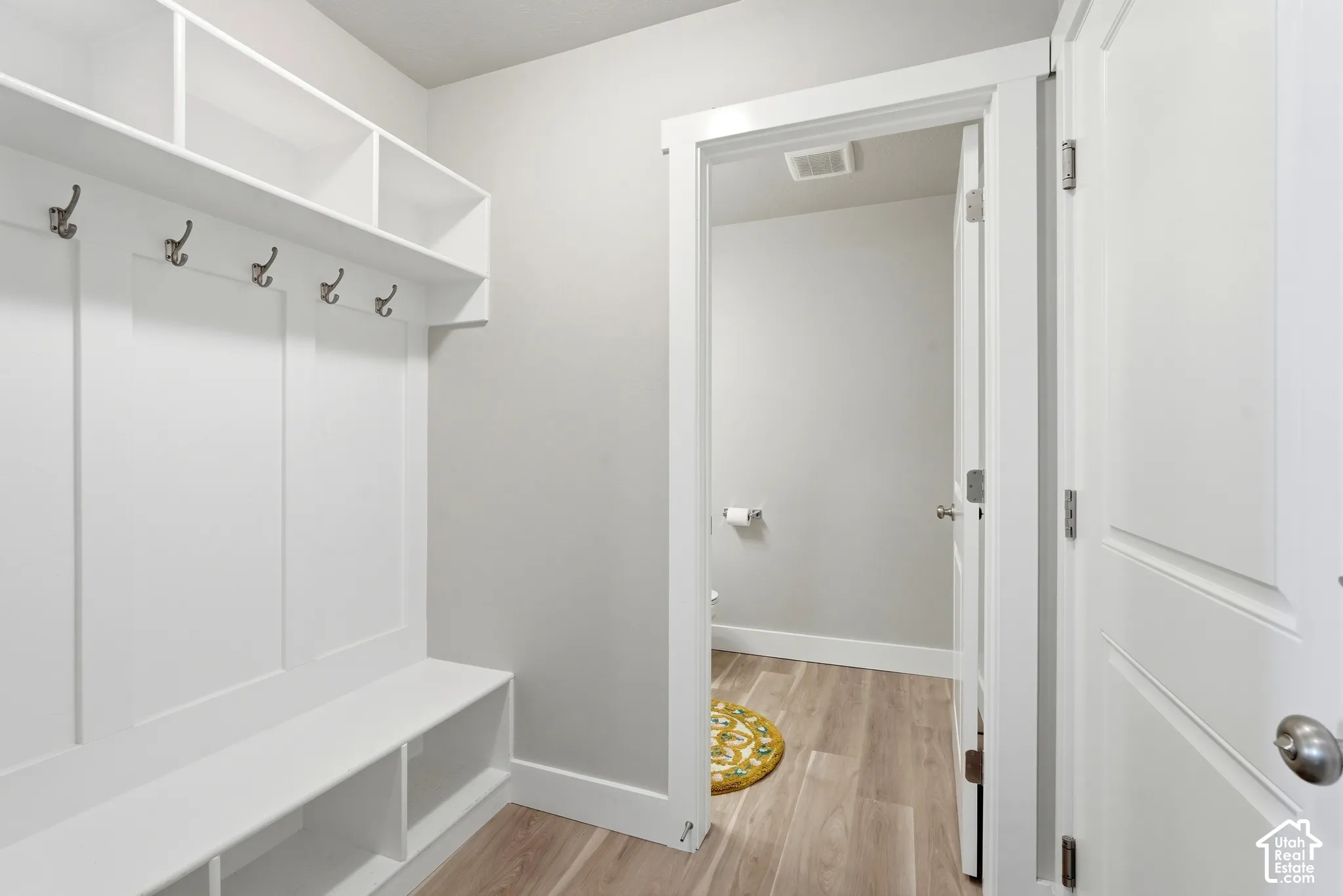 Built-in white storage unit featuring a bench, open shelving, and coat hooks