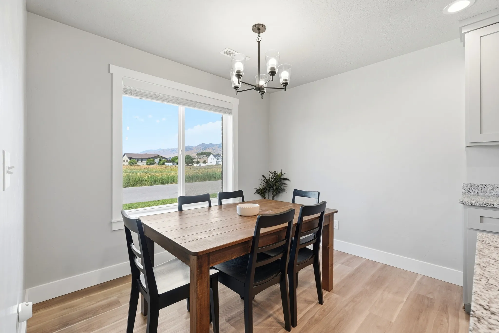 Dining area featuring a large window, light wood-finish flooring, a contemporary chandelier, and light gray cabinetry with a granite countertop