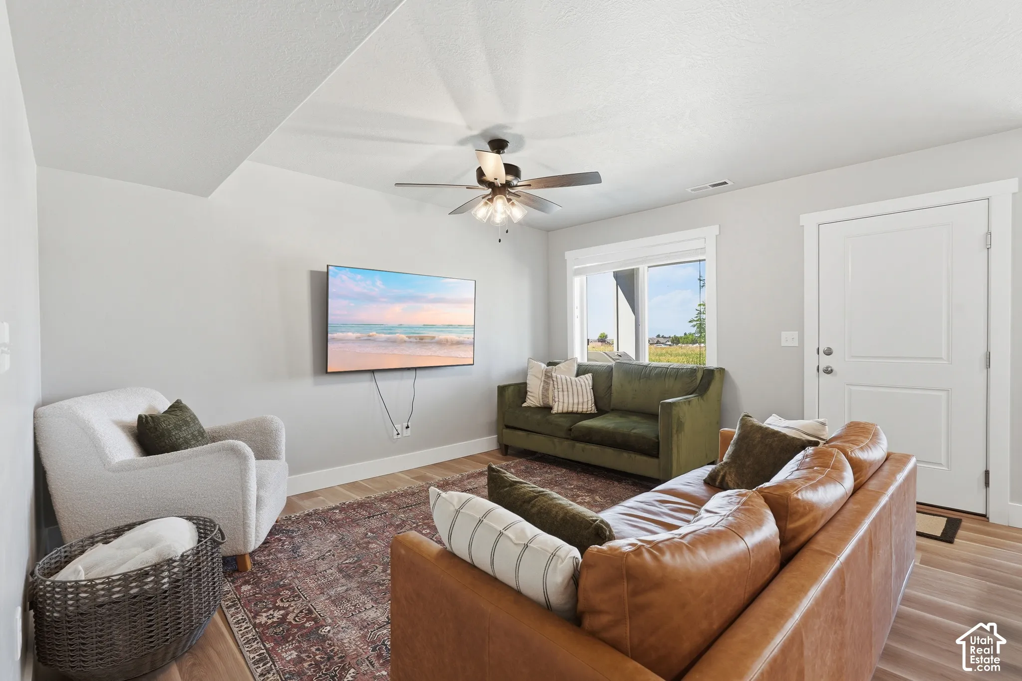 Open-concept living space with light gray walls, wood-finish flooring, and a ceiling fan