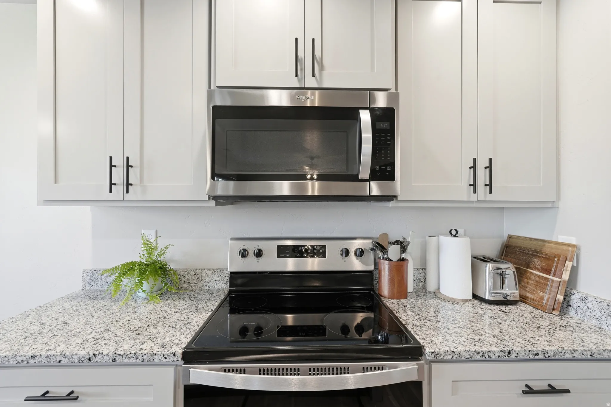 Kitchen featuring light gray cabinetry, stainless steel appliances, speckled stone countertops, and black hardware