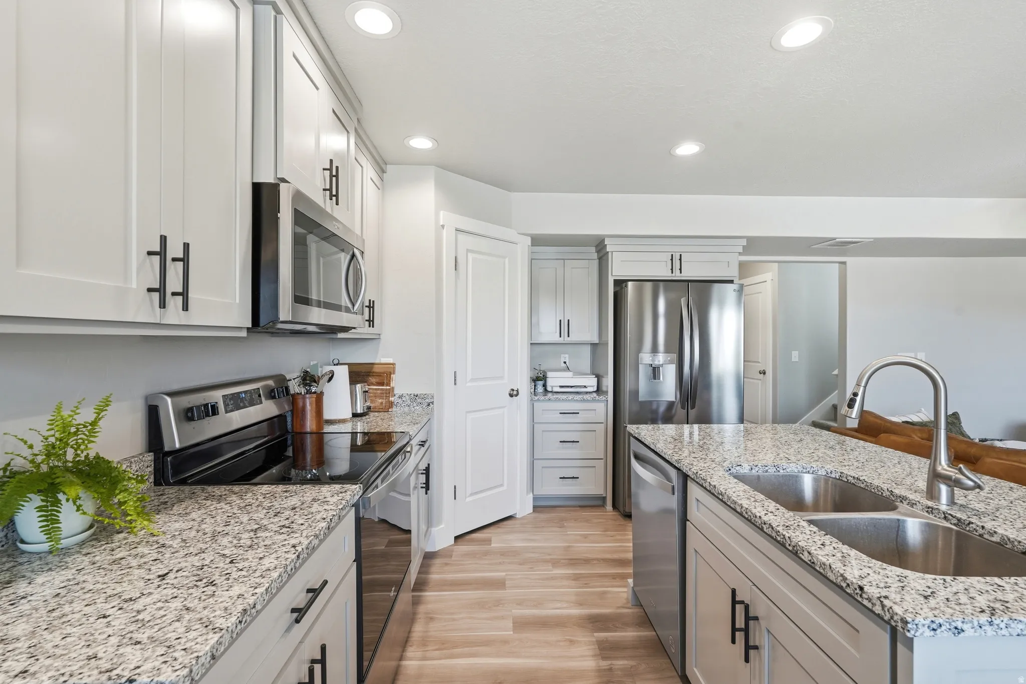 Modern kitchen featuring light cabinetry with dark hardware, speckled countertops, stainless steel appliances, and wood-finish flooring