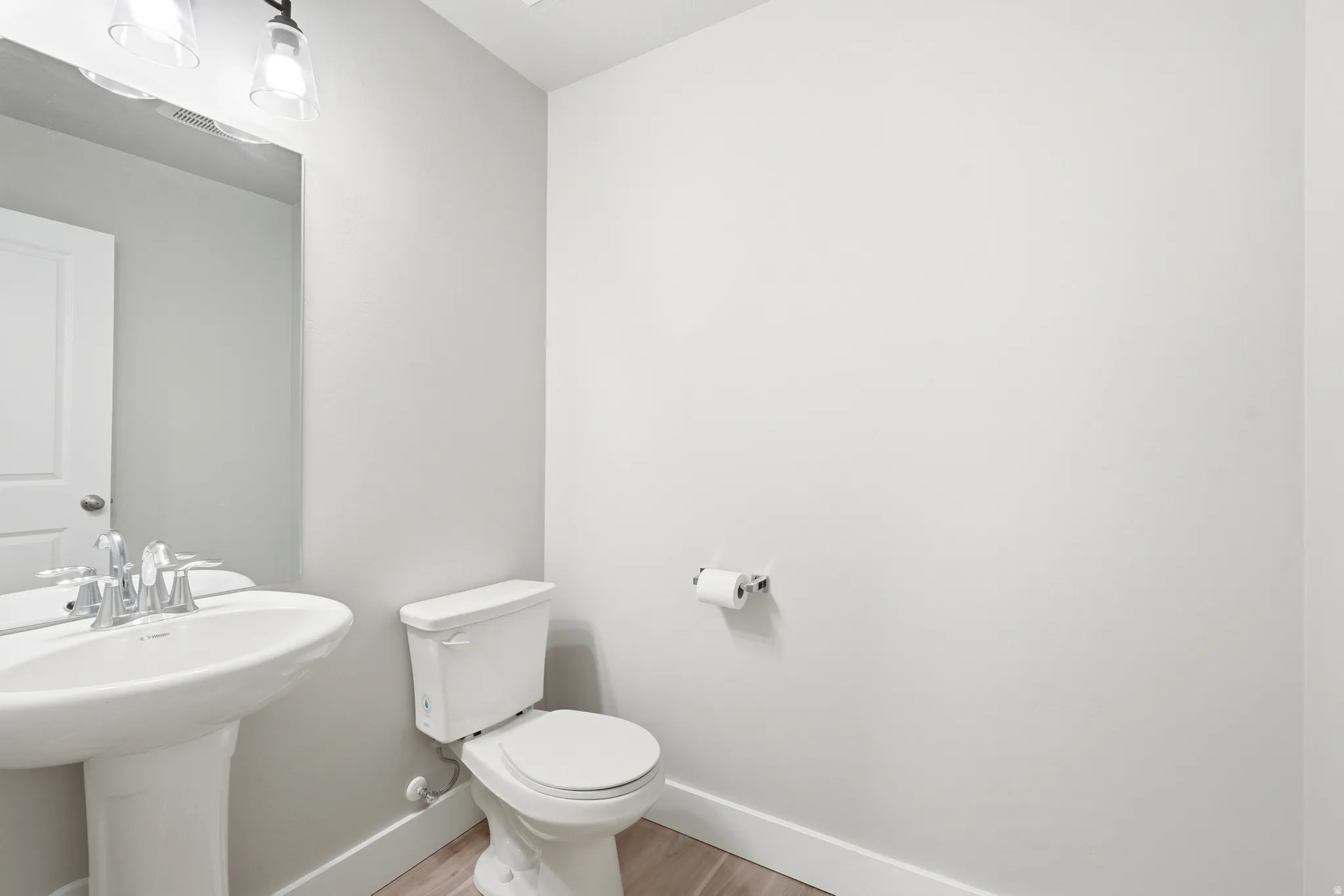 Powder room featuring a pedestal sink with chrome faucet, a white toilet, and wood-finish flooring