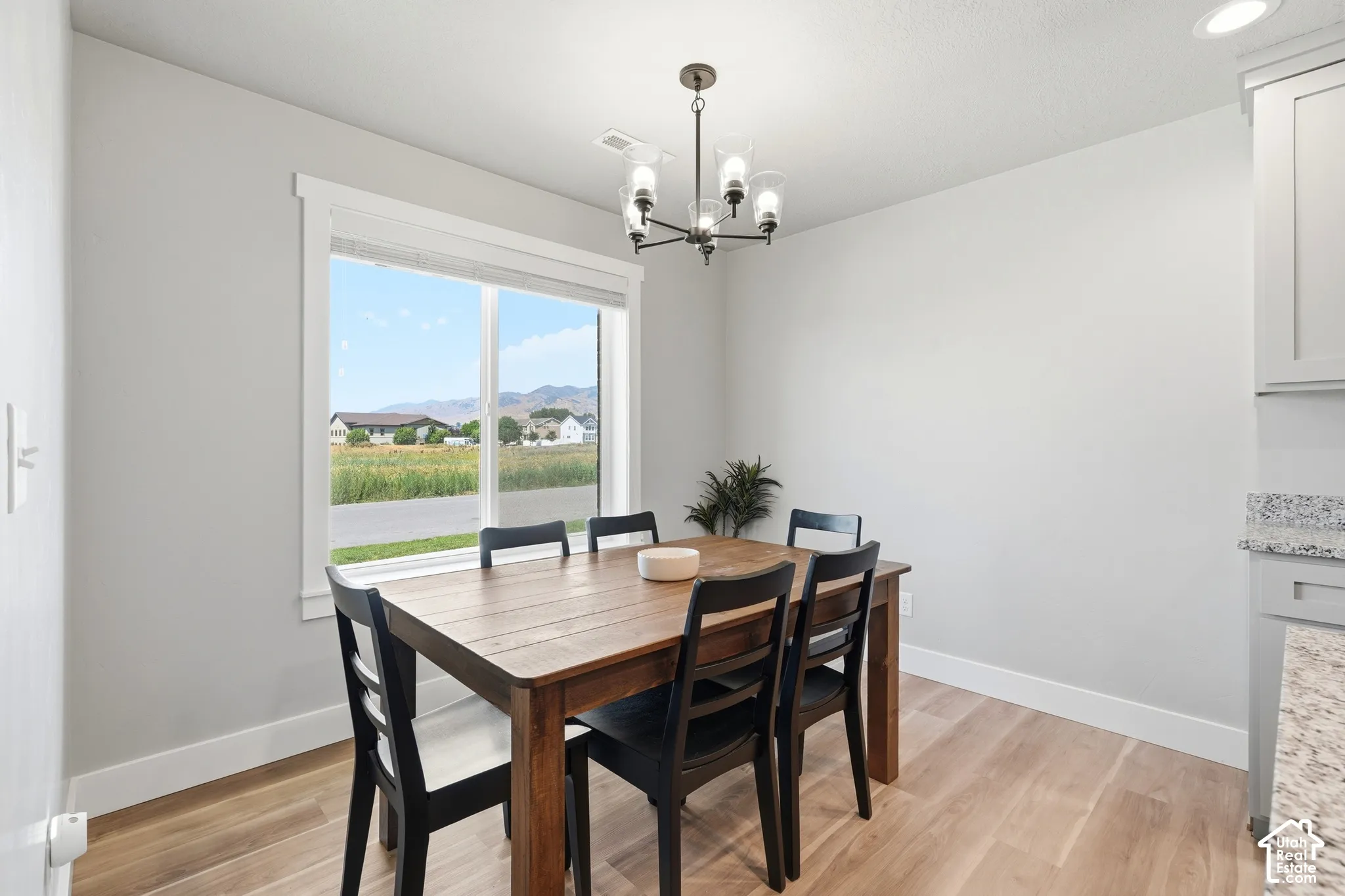 Dining area featuring a large window, light wood-finish flooring, a contemporary chandelier, and light gray cabinetry with a granite countertop