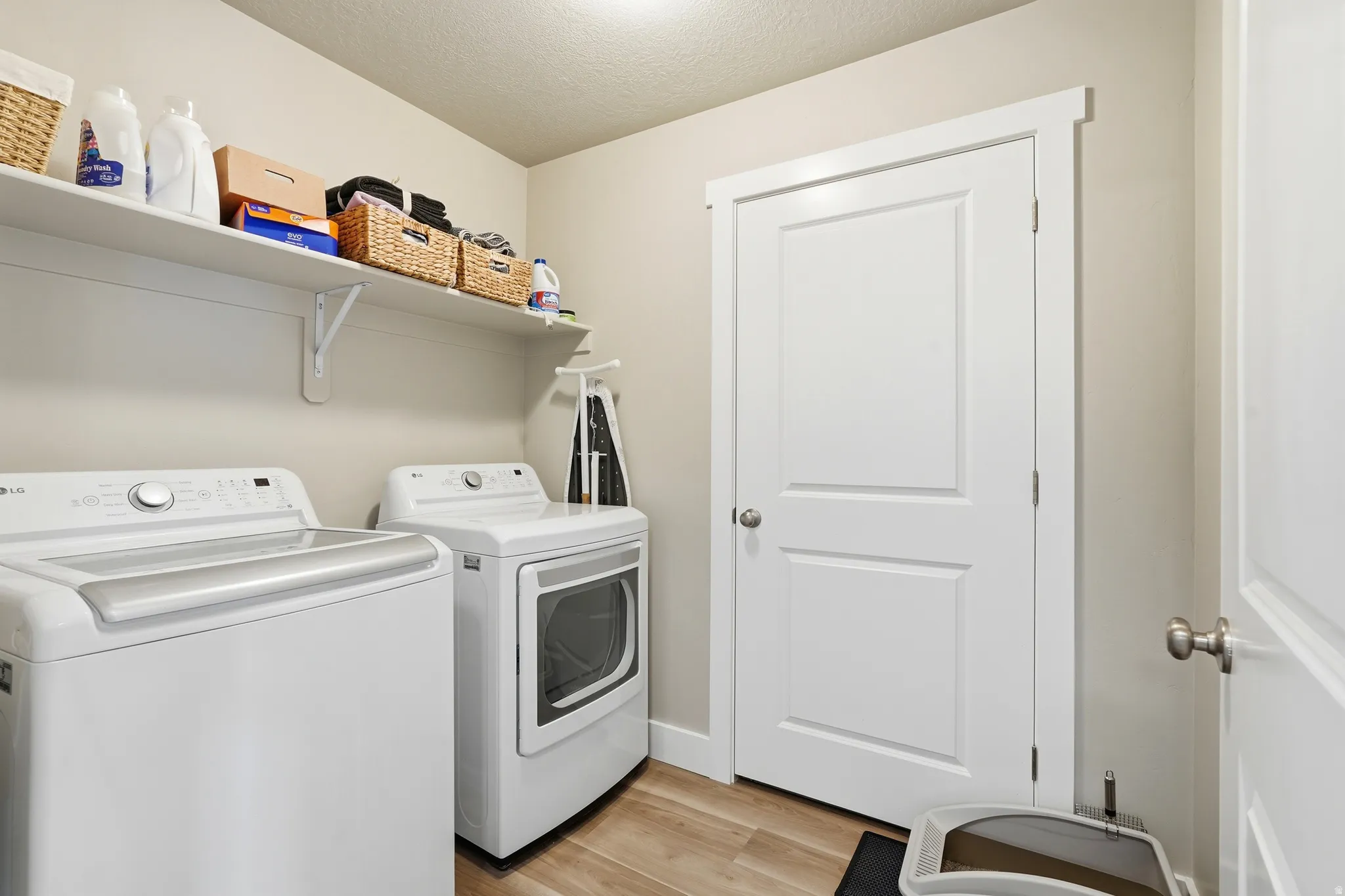 Functional laundry area featuring light wood-finish flooring, light neutral wall paint, and white trim molding
