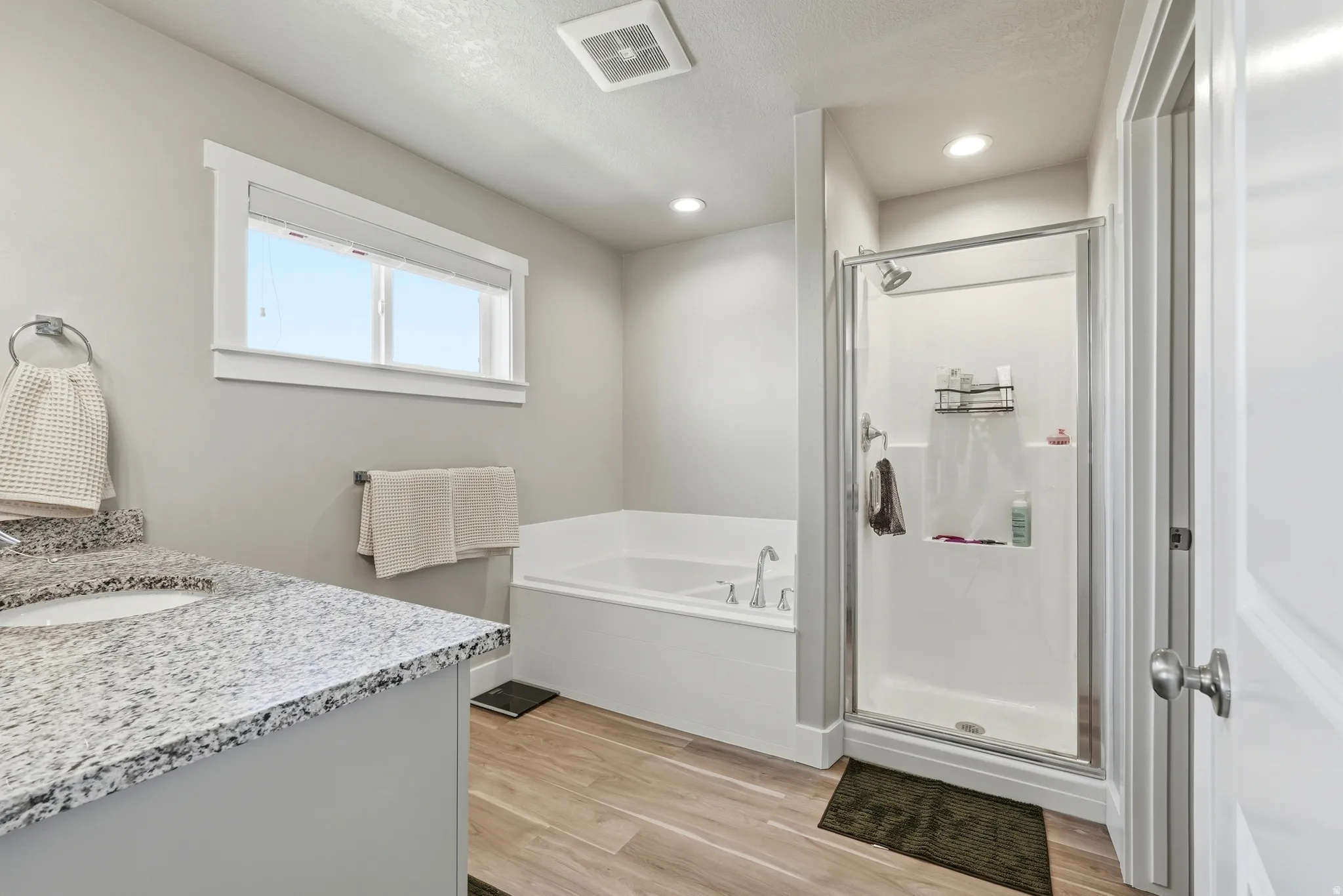 Primary Bathroom featuring a built-in soaking tub, glass-enclosed shower, single vanity with a granite-style countertop, and wood-finish flooring