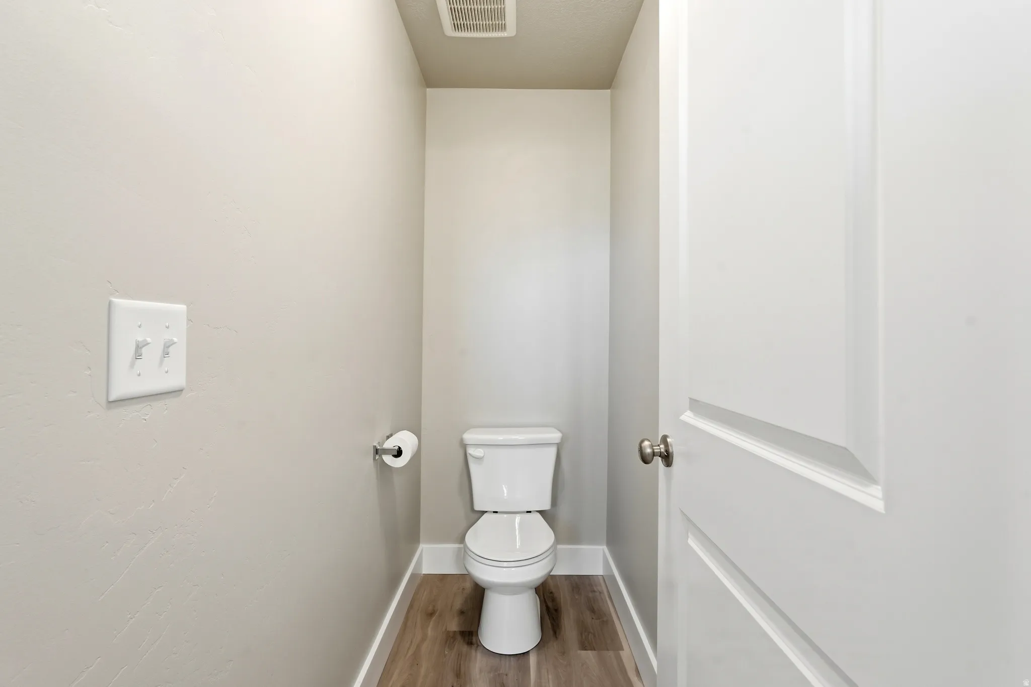 Primary toilet room featuring neutral wall tones, white trim, wood-finish flooring, and a panel-style door