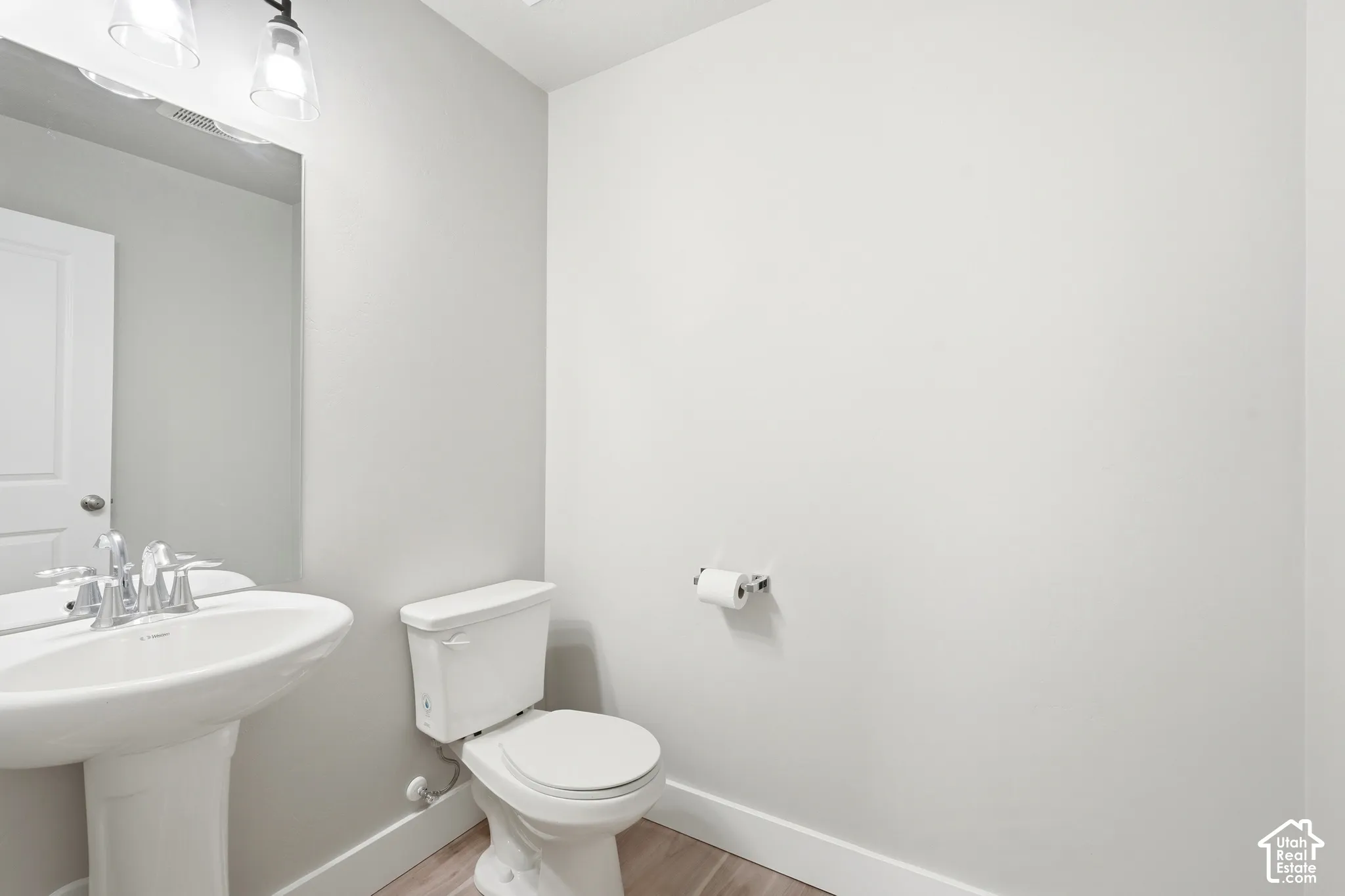Powder room featuring a pedestal sink with chrome faucet, a white toilet, and wood-finish flooring