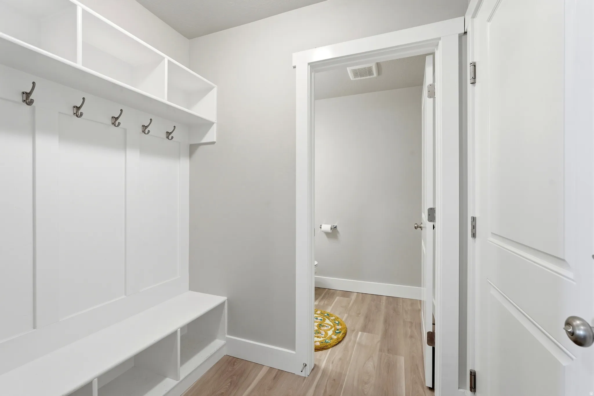Built-in white storage unit featuring a bench, open shelving, and coat hooks