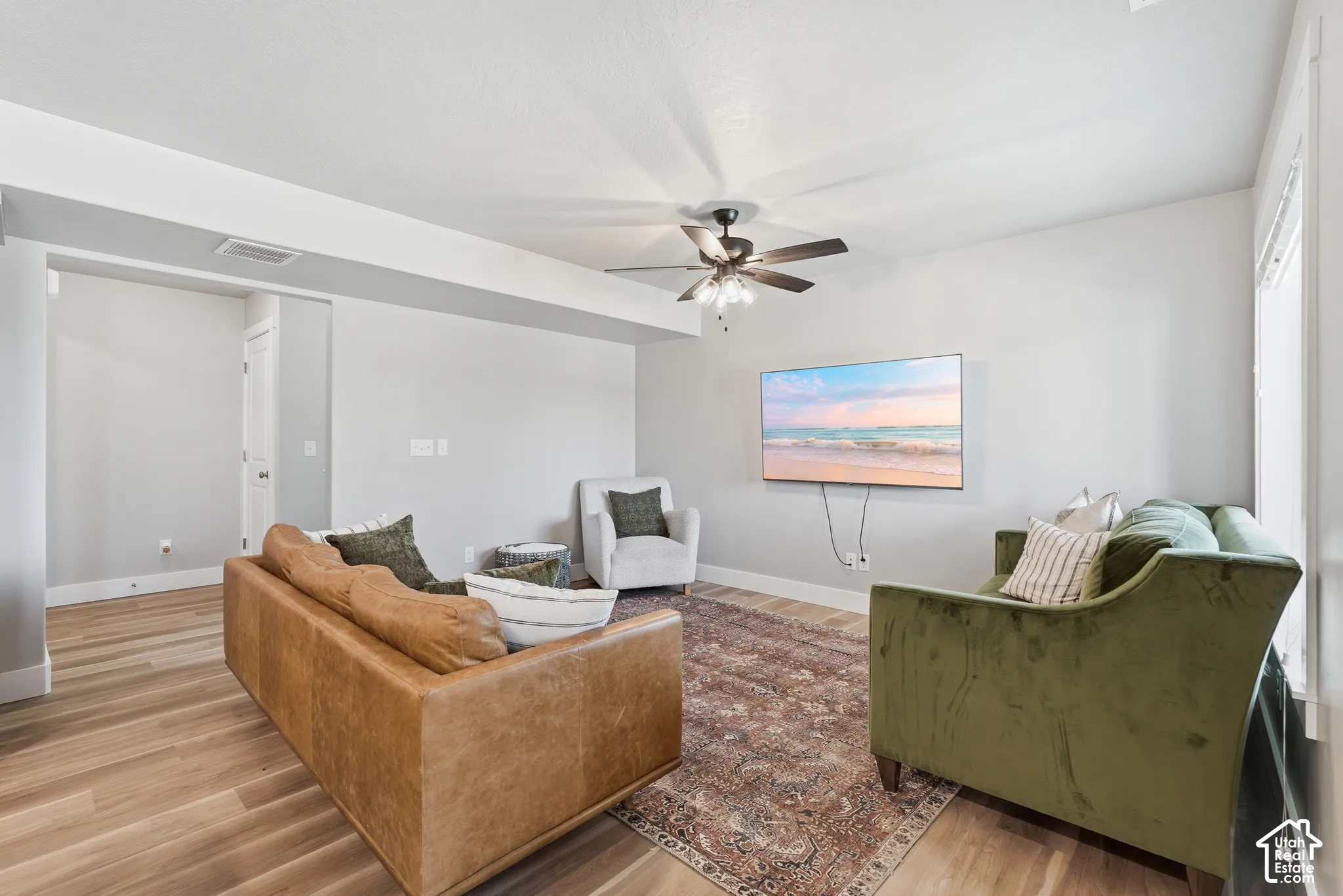 Spacious living area featuring wood-finish flooring, a ceiling fan, light gray walls, white trim, and an open entryway