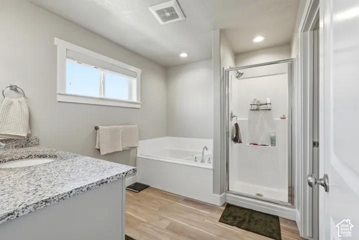 Primary Bathroom featuring a built-in soaking tub, glass-enclosed shower, single vanity with a granite-style countertop, and wood-finish flooring