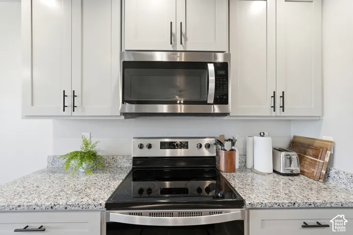 Kitchen featuring light gray cabinetry, stainless steel appliances, speckled stone countertops, and black hardware