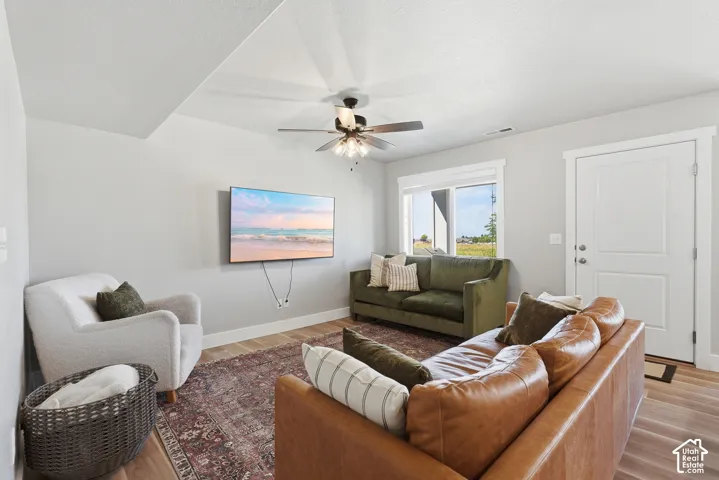 Open-concept living space with light gray walls, wood-finish flooring, and a ceiling fan
