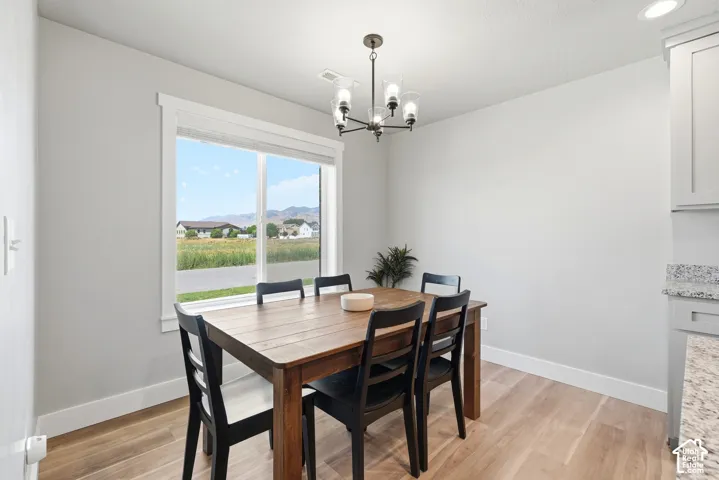 Dining area featuring a large window, light wood-finish flooring, a contemporary chandelier, and light gray cabinetry with a granite countertop