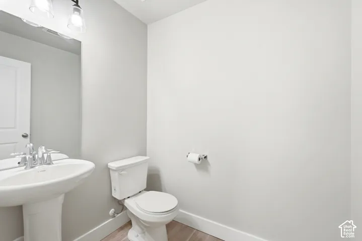 Powder room featuring a pedestal sink with chrome faucet, a white toilet, and wood-finish flooring