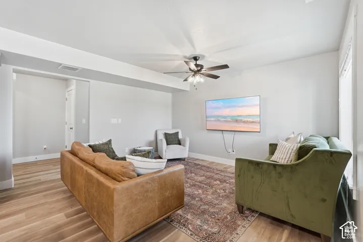Spacious living area featuring wood-finish flooring, a ceiling fan, light gray walls, white trim, and an open entryway
