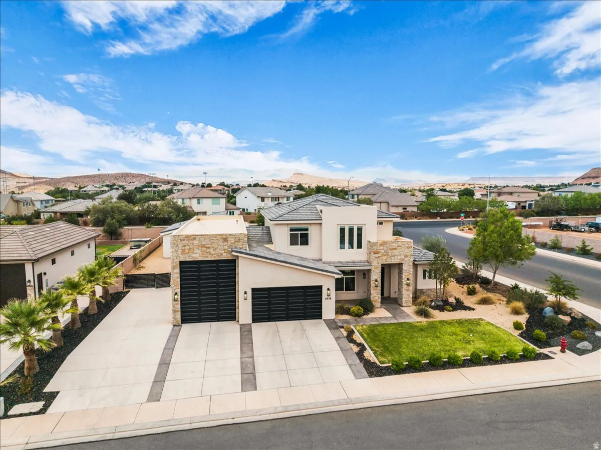 Contemporary stucco and stone exterior featuring multiple garage bays with dark horizontal panel doors, a manicured lawn area, and a paved driveway with dark accent strips