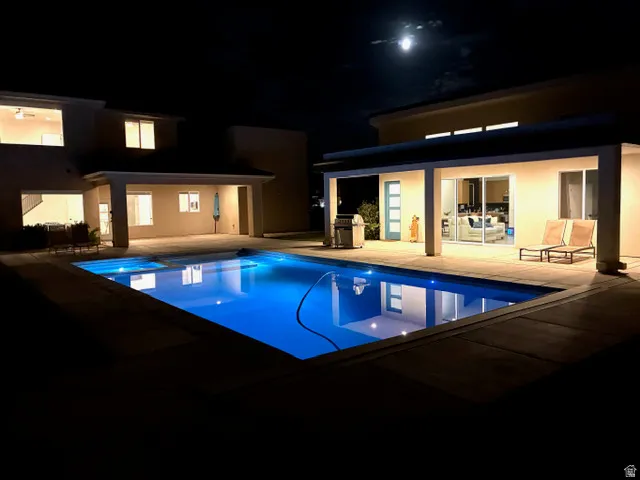 Illuminated rectangular swimming pool with integrated spa, surrounded by expansive concrete decking