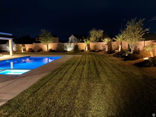 Expansive backyard featuring a rectangular swimming pool with integrated spa, a large lawn area, and perimeter landscaping with mature trees