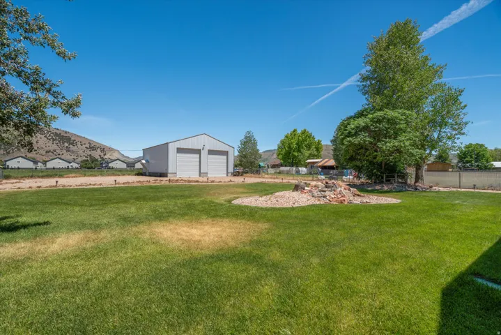 Expansive grassy yard featuring a dedicated rock garden, mature trees, and a detached two-bay garage with roll-up doors