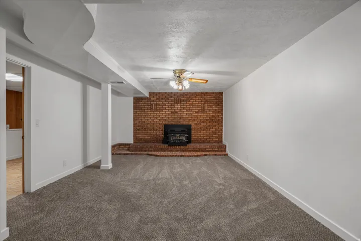 Spacious room with new gray carpeting, a brick accent wall with fireplace, and a ceiling fan