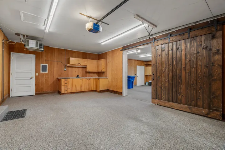 Spacious garage with epoxy flooring, paneled wood walls, built-in cabinetry, and a large wood barn door