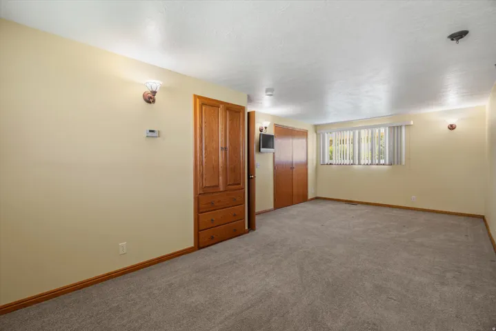 Carpeted room featuring a window with vertical blinds, two built-in wood-finish closets, and two wall-mounted sconces
